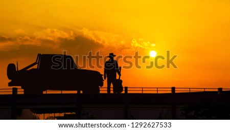 The young man standing holding the guitar looking at the sun is falling beside the pickup truck. silhouette,
