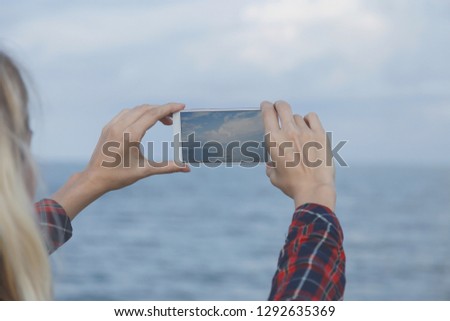 beautiful girl takes pictures of the sea. Women's hands, holding the smartphone