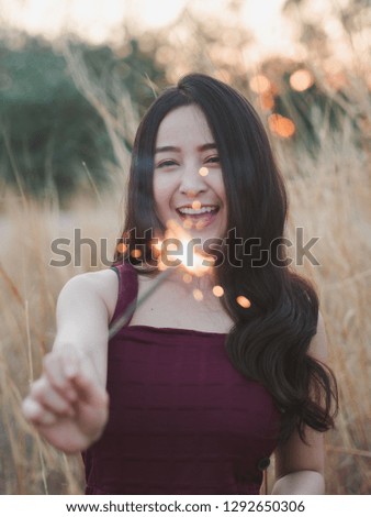 Happy cute girl holding a sparkler in the dry grass field for celebrate.