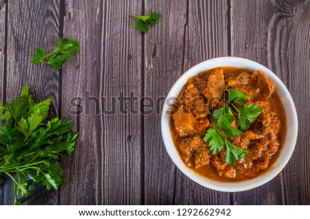Freshly cooked veal goulash with parsley in a deep white plate on a dark wooden background. Food photography