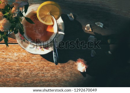 Still life image of cup of rose tea with honey and lemon on wooden background.Hot tea with vapor and steam in a cup.Light shining up on the scene.Quiet,peace and relax.