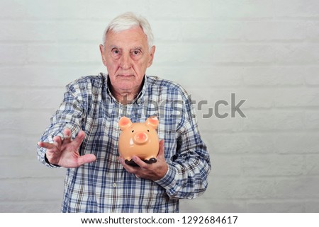 senior man with a piggybank on brick background Royalty-Free Stock Photo #1292684617