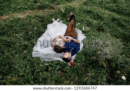 lovers - a bride in a dress and a groom in a blue shirt and with a beard are lying on the grass in the forest and gently hugging, a wedding photo for Valentine's Day