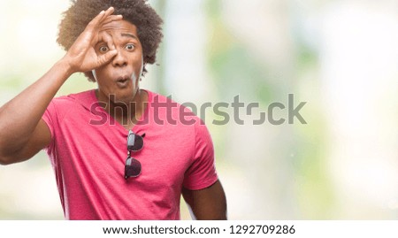 Afro american man over isolated background doing ok gesture shocked with surprised face, eye looking through fingers. Unbelieving expression.