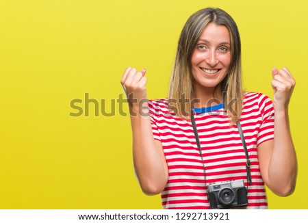 Young beautiful woman taking pictures using vintage photo camera over isolated background celebrating surprised and amazed for success with arms raised and open eyes. Winner concept.