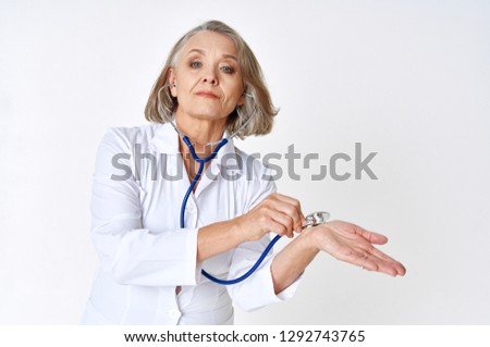elderly female doctor leaning a stethoscope in the white coat on a light background