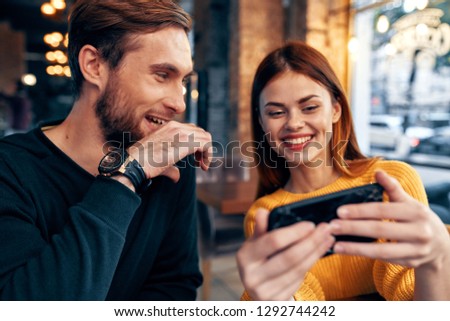 Cheerful nice couple sitting in a cafe looks into the phone