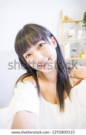 An Asian woman sits on the bed and takes a selfie by camera. This is lifestyle.
