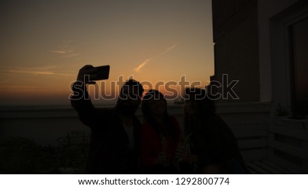 Hipster man taking picture with his smart phone with two girls at the sunset