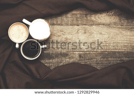 A cup of black coffee and coffee with cream on a wooden background. Bowl with cream. Brown coverlet. Top view