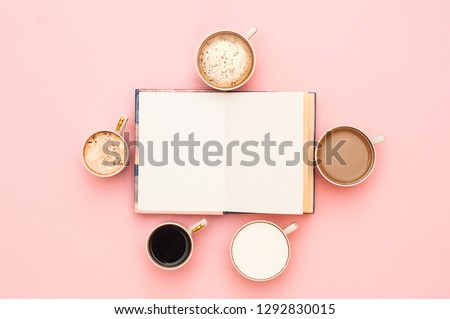 Many cups of coffee and an open book on a gently pink background. Top view