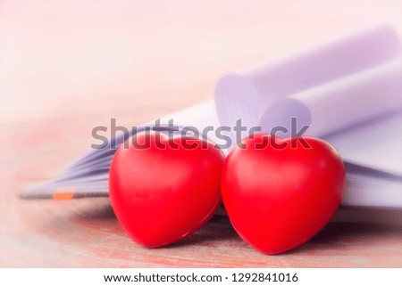 Valentine's day holiday and love concept. Vintage style picture of couple of red hearts shape, blank white book on wooden table background.