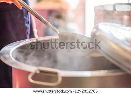 Cooking person in the restaurant is cooking while using the dipper in a large pot. And the water is boiling.