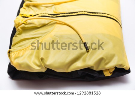 Folded yellow zipper windbreaker jacket, rain proof jacket hoodie. Track jacket sport shiny nylon full zip isolated on white. Folded clothes.