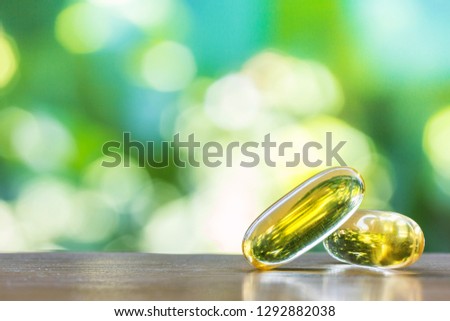 fish oil supplement capsules in selective focus on top wooden table with green natural bokeh background