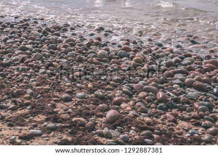 rock covered beach in countryside in Latvia, large rocks in water with calm wind and sunshine - vintage retro film look