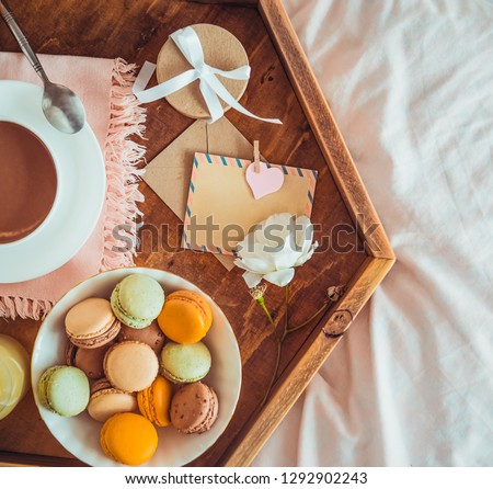 Breakfast in bed with empty blank card. Cup of coffee, juice, macaroons, flower and giftbox on wooden tray. Romantic breakfast in bed. Birthday, Valentine's day morning. Top view. Square. Copy space