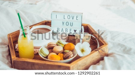 Romantic Breakfast in bed with I love you baby text on lighted box. Cup of coffee, juice, macaroons, flower and gift box on wooden tray. Birthday, Valentine's day morning. Wide banner. Copy space