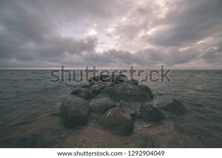 storm clouds forming over clear sea beach with rocks and clear sand. dramatic colors - vintage retro film look
