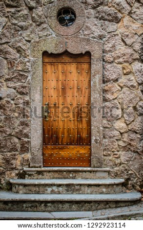 Old wooden door with stairs in front of it and stone wall near Quinta da Regaleira in Sintra, Lisbon, Portugal
