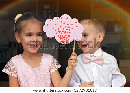 Little boy in white shirt and pink bow-tie and beautiful princess wearing soft dress holding signs with a lot of hearts, they fall in love, romantic and love concept, Valentine Day greeting