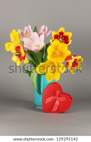 Beautiful tulips in bucket with gift on grey background