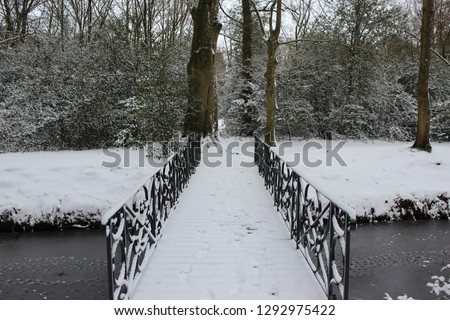 Snow covered footpath bridge over stream in a park