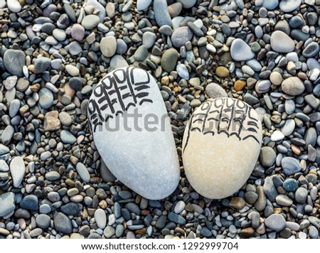 Two traces of the feet made of sea stones, fingers drawn with a marker on background pebbles sea on the beach