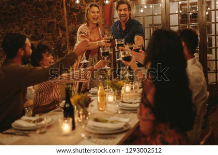 Group of friends toasting drinks at a party. Young people hanging out at dinner party and having drinks.