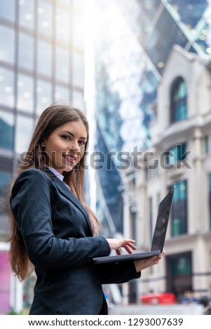Attractive businesswoman working on laptop outdoors in the City fo London and looking into the camera