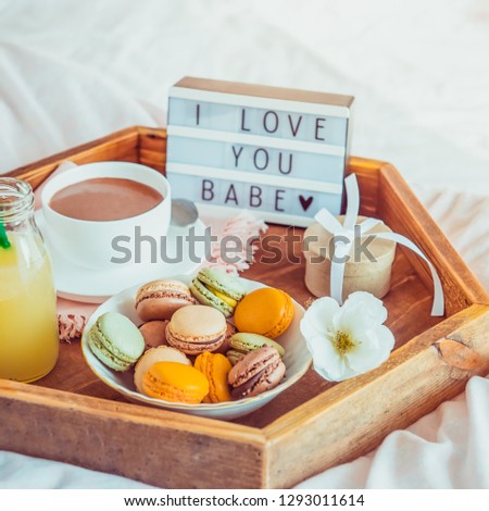 Close up Romantic Breakfast in bed with I love you baby text on lighted box. Cup of coffee, juice, macaroons, flower and gift box on wooden tray. Birthday, Valentine's day morning. Square. Copy space