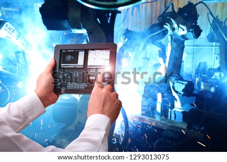 Industry 4.0 ,  concept  of Man hand holding cell phone or tablet with Augmented reality screen software and blue tone of automate wireless Robot arm in smart factory background. Mixed media