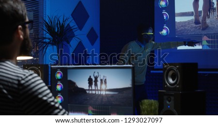 Medium shot of young man editing video inside a modern video studio while his colleague is giving instructions