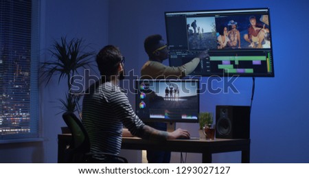 Medium shot of a young man editing video inside the room while his colleague is giving instructions