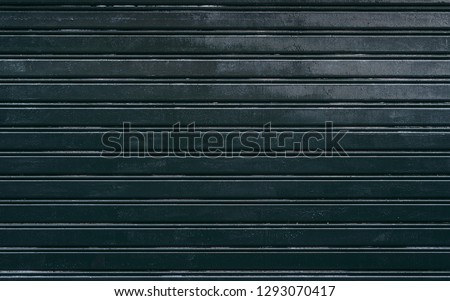 The dark-green surface of an outdoor metallic vertical folding door from a street shop or a garage, texture consists of thick horizontal stripes and smaller vertical lines inside