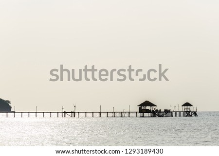 long wooden bridge in the sea with old wooden hut and white sky background