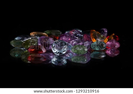 Group of transparent diamond shaped stones in all kinds of colours on a reflecting surface surrounded with a black studio background