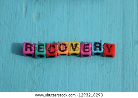 Recovery words spelled out in primary colors colorful abc alphabet beads blocks on blue wood background.