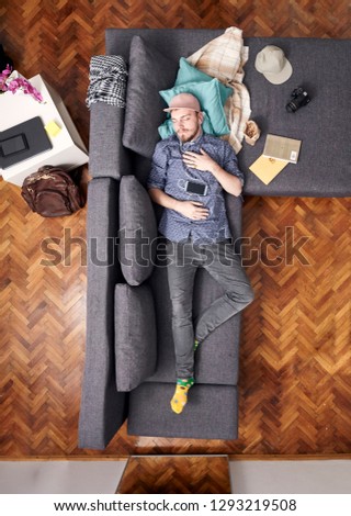 one young hipster man, laying in bed sleeping. whole sofa and bed visible, view from above.