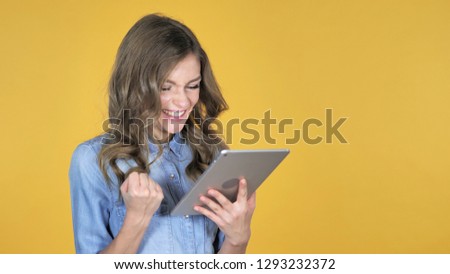 Young Girl Excited for Success while Using Tablet Isolated on Yellow Background