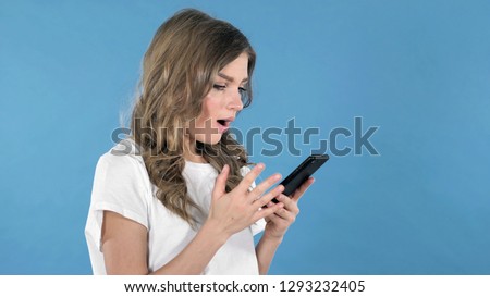Young Girl Excited for Success while Using Smartphone Isolated on Blue Background