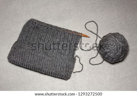 process of knitting men's hats with an elastic band with a lapel and a round crown of gray acrylic, a warm stylish winter hat