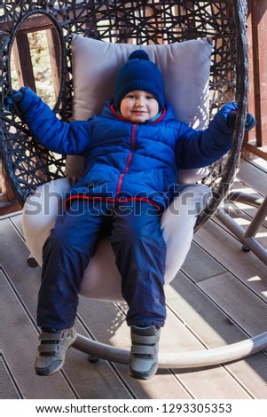 happy four year old boy lying in hanging wicker chair outdoors in spring