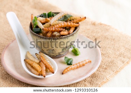 Food Insects: Bamboo worm (Bamboo Caterpillar) insect fried crispy for eating as food items on dish and spoon on sackcloth, it is good source of protein edible for future food. Entomophagy concept. Royalty-Free Stock Photo #1293310126