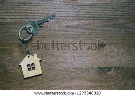 Symbol of a bamboo house with a metal key on a brown vintage wooden background. Lighting gradient. The concept of selling real estate with the transfer of ownership.