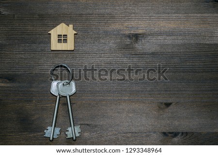 Symbol of a bamboo house with a metal keys on a brown vintage wooden background. Lighting gradient. The concept of selling real estate with the transfer of ownership.