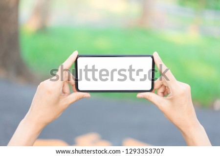 Hand holding smartphone with white screen on nature background.