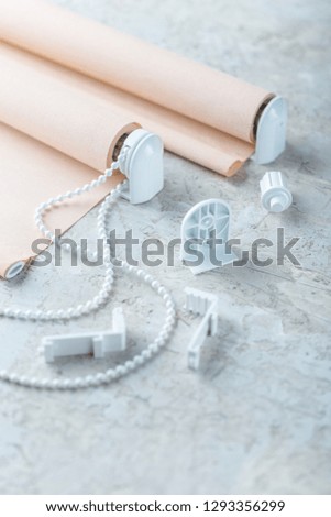 The roller blind lies on a white or gray concrete surface.