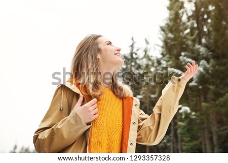 Young woman in warm clothes catching snow outdoors. Winter vacation