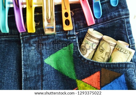 A jean trouser hung with  clothespins with rolling dollar bank notes in a pocket.